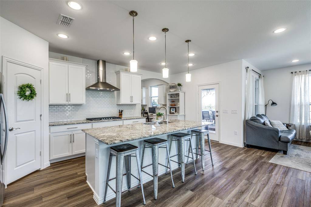 Kitchen featuring wall chimney range hood, stainless steel gas cooktop, a sink, white cabinetry, and a kitchen breakfast bar