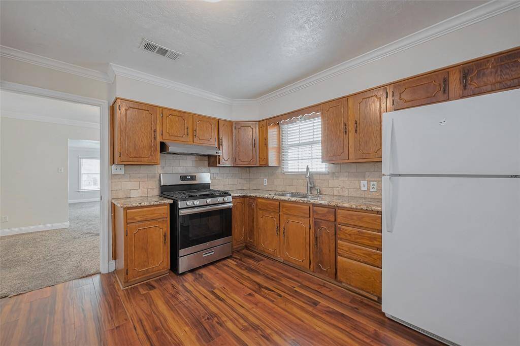 Dark wood-like flooring enhances the kitchen’s warmth, while elegant crown molding adds a refined touch to the space.