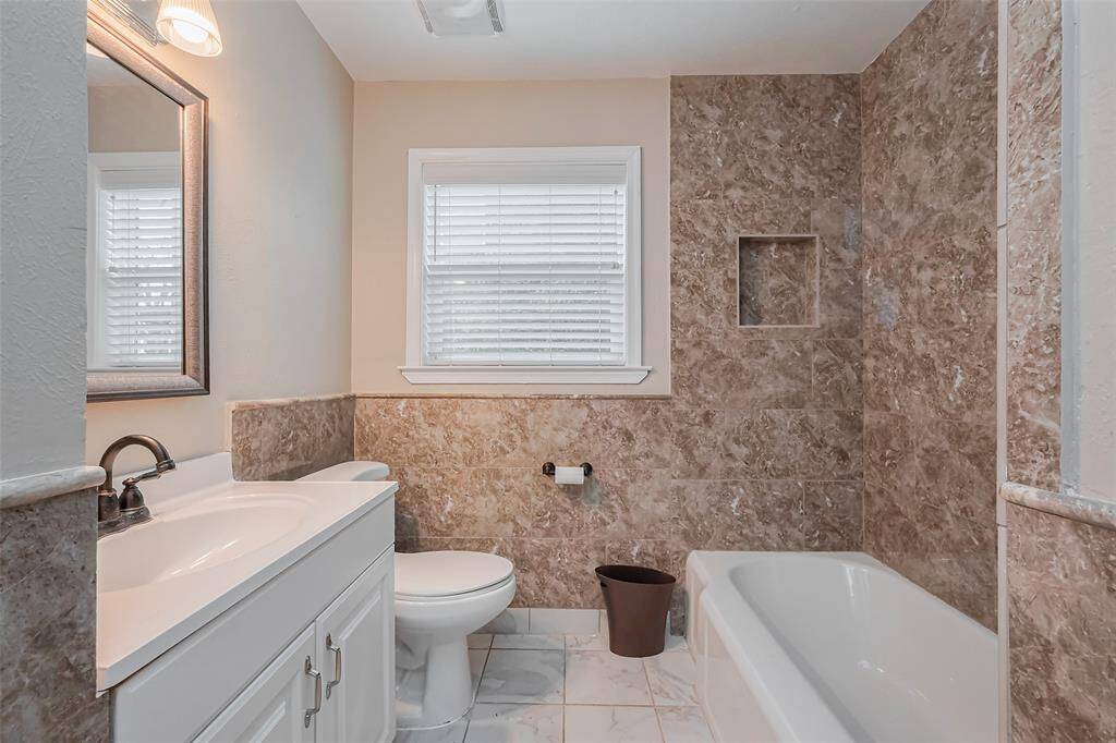 This primary bathroom is designed for both relaxation and convenience, featuring a tub/shower combination surrounded by stylish tiling.