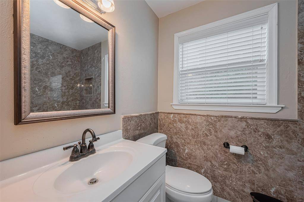 A bright and well-lit vanity area includes a large mirror and under-sink storage. A window allows for natural light, creating a fresh and inviting atmosphere.