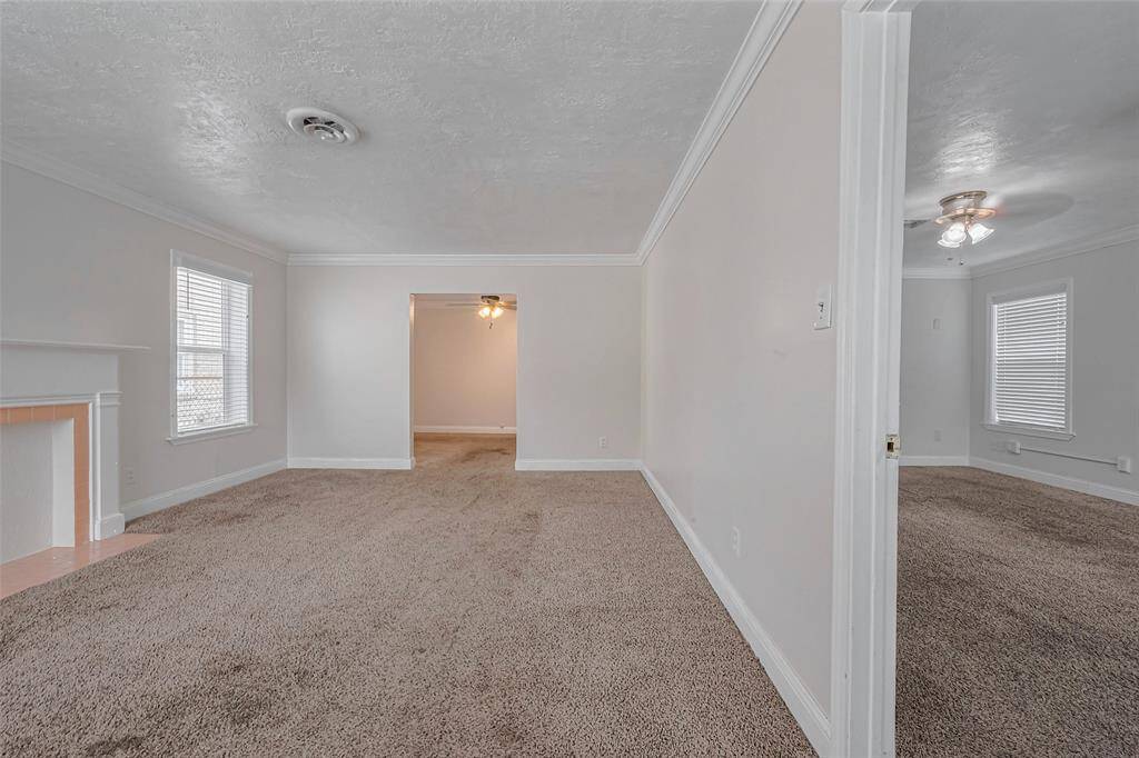 Step inside to an expansive carpeted living area that immediately feels inviting. To the right, the doorway leads to the primary bedroom, while the neutral palette and fresh paint enhance the sense of brightness throughout.