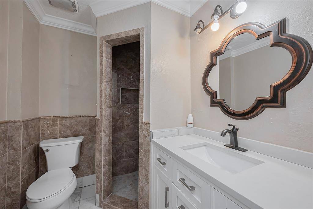 The secondary bathroom features excellent lighting, a large mirror, and a white vanity with built-in storage.