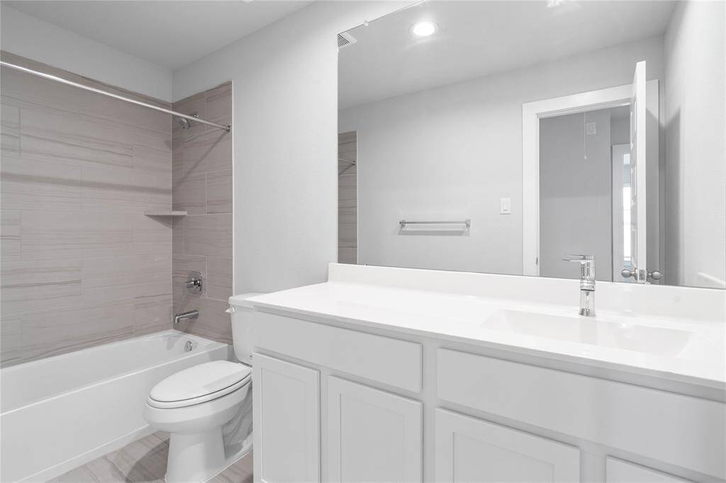 Secondary bath features tile flooring, bath/shower combo with tile surround, stained cabinets, beautiful light countertops, mirror, sleek fixtures and modern finishes.