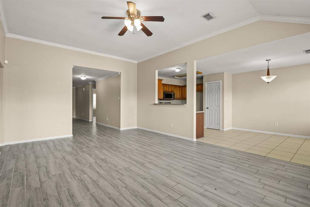 This spacious living area features light wood-style flooring. Bright and inviting atmosphere,  seamlessly connecting to a tiled dining area and a kitchen with stainless steel appliances and warm wooden cabinetry. A ceiling fan adds comfort and style.