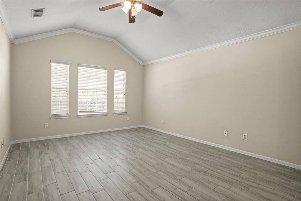 This room features a vaulted ceiling with a ceiling fan and wood-look tile flooring. Three windows provide ample natural light, creating a spacious and inviting atmosphere.