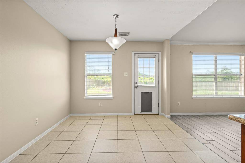 Bright dining area with modern light fixture. Large windows and a glass door provide ample natural light, leading to an outside view of the backyard. The space opens to the living area.