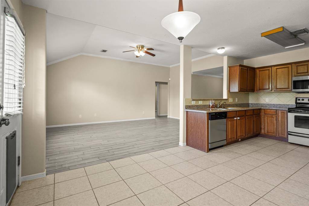 This spacious open-concept area features a kitchen with wooden cabinets, stainless steel appliances, and tiled flooring. It seamlessly transitions into a large living space with wood-look flooring and a ceiling fan, ideal for entertaining.