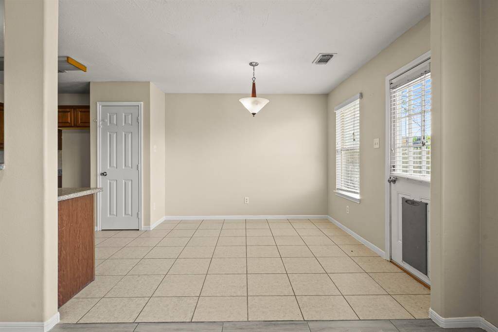 This photo features a tiled dining area with a hanging light fixture. It has a door with a window leading outside to the backyard.