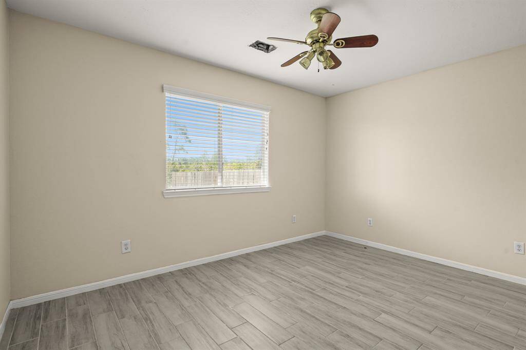This photo showcases a bright room with  wood-like tile flooring. It features a window with blinds and a ceiling fan, creating a comfortable space.