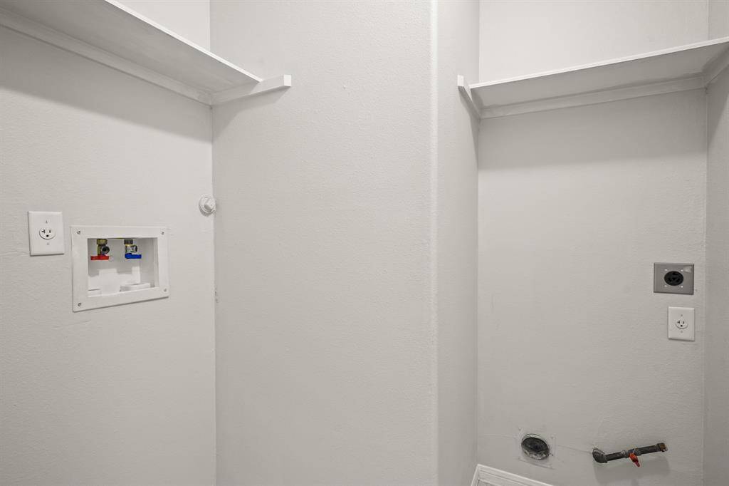 This photo shows a laundry area with hookups for a washer and dryer along with selves above for storage.