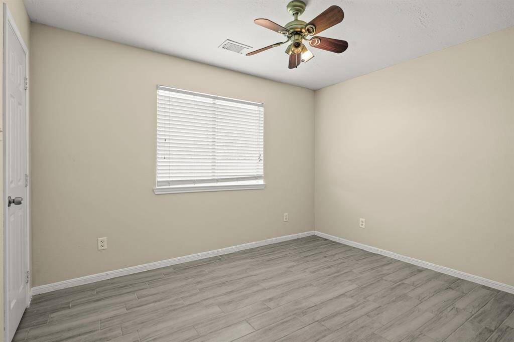 This room features  a ceiling fan, and natural light from a window. It has sleek hardwood-style flooring.