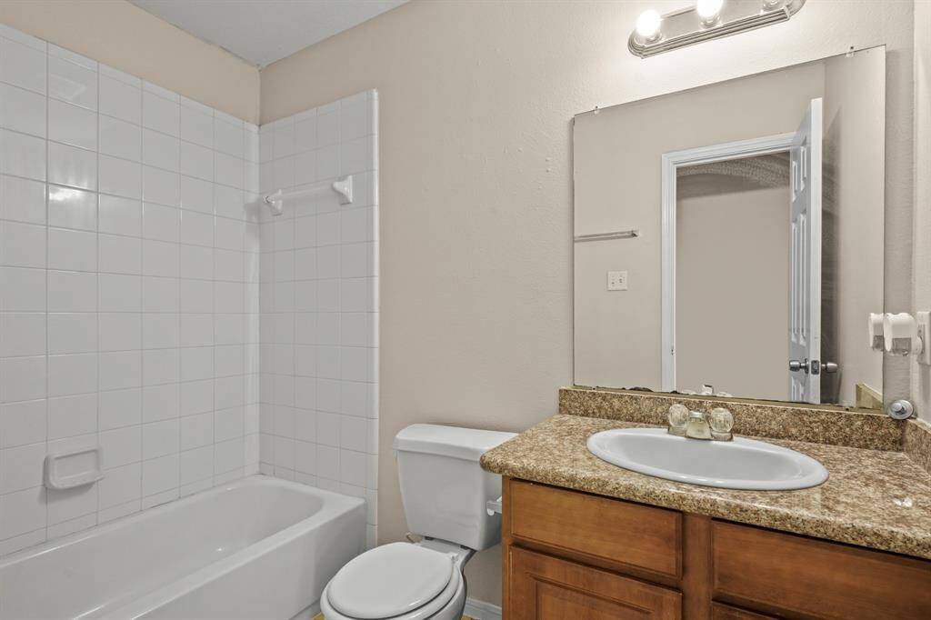 This bathroom features white tiled shower and bathtub combination, a granite countertop with one sink and a large mirror.