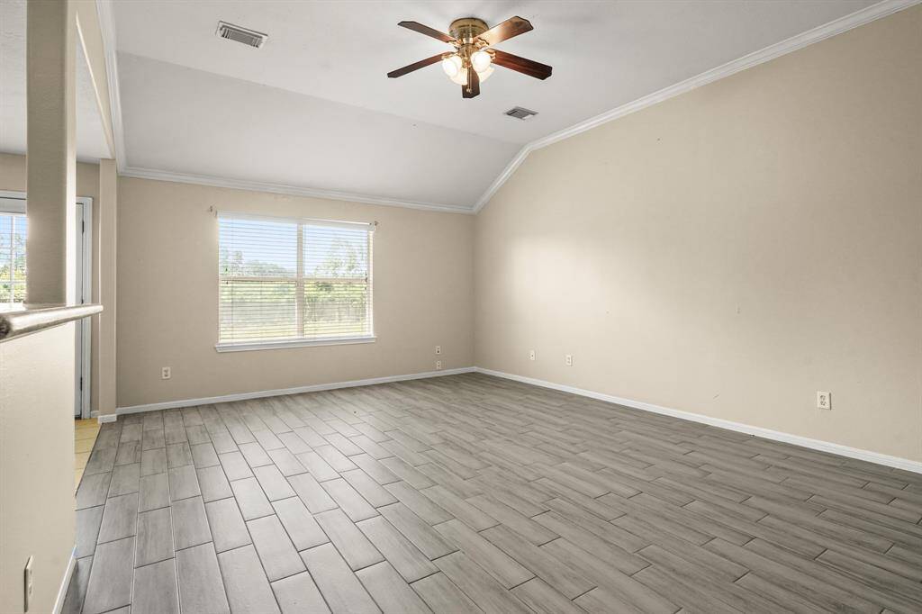 Bright living area with high ceilings,  and wood-style tile flooring. Features a ceiling fan and large windows for natural light with view to back yard.
