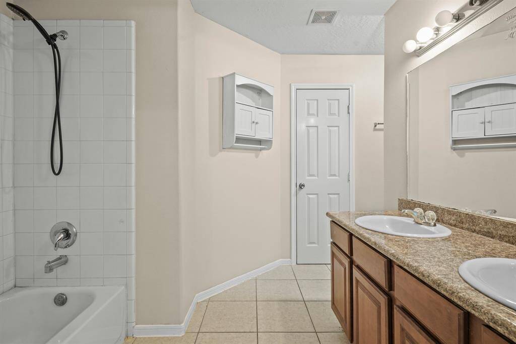 This spacious bathroom features a dual-sink vanity with granite countertops, a full bathtub with shower, tiled floors, and ample storage options.