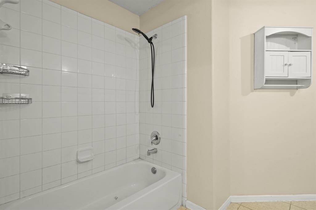 This bathroom features a tiled bathtub with a modern showerhead and built-in shelving for storage. A wall-mounted cabinet provides additional space.