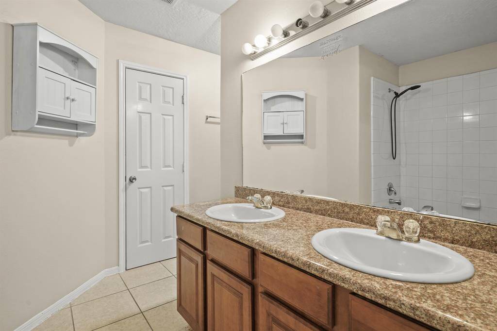 This bathroom features a double sink vanity with a granite countertop, ample storage, and a large mirror. It includes a tiled bathtub with a shower.