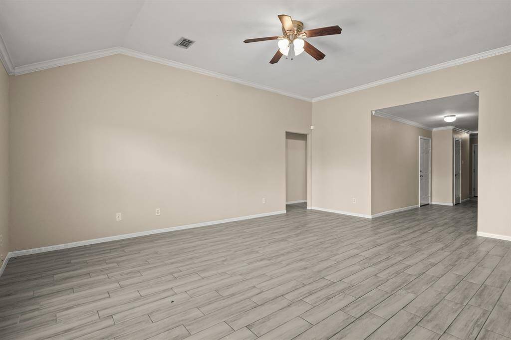 Spacious living area features a  ceiling fan and crown molding. The open layout leads to a hallway, offering a versatile space for various setups.