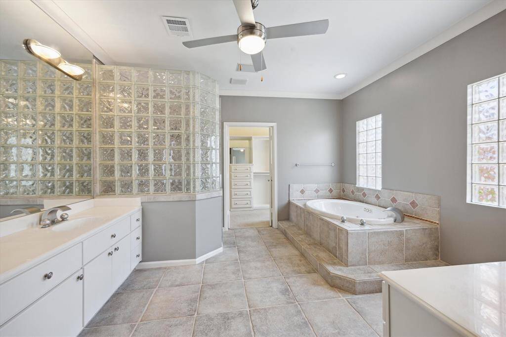 Primary bathroom with double sinks, one set on the left and another one on the right, out of sight, with a spa tub on the right, shower on the left, and the closet straight ahead.
