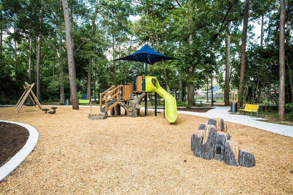 Charming community playground surrounded by trees, featuring a play structure with a slide, shaded seating, and a peaceful walking path. Ideal for families seeking a serene neighborhood environment.