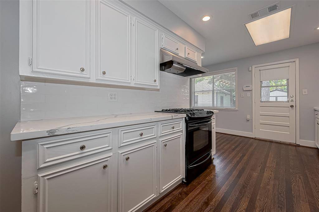 This room features hardwood flooring, neutral walls, and a ceiling fan with lights. It has two windows with shades, providing natural light. The space is simple and versatile, ideal for a bedroom or office.