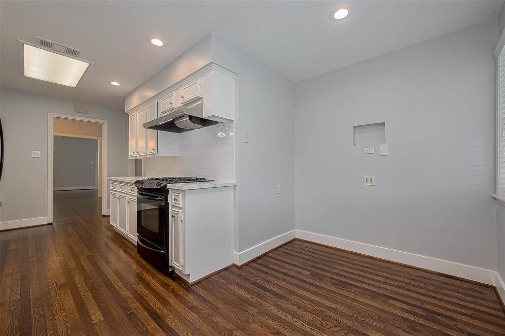 This kitchen features bright white cabinetry with modern fixtures, a built-in microwave, and a sleek black dishwasher. The countertops are spacious, and the hardwood floors add warmth to the space.