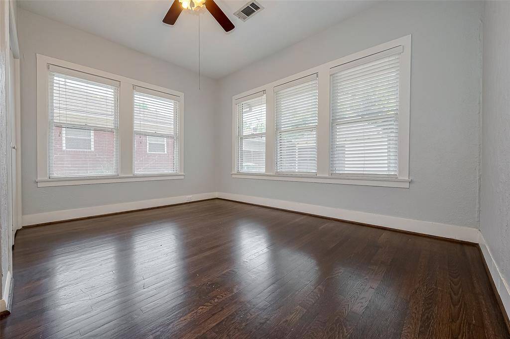 This kitchen features sleek white cabinetry, dark hardwood floors, and modern appliances, including a black dishwasher. A door with a window and a large sink under a window provide ample natural light.