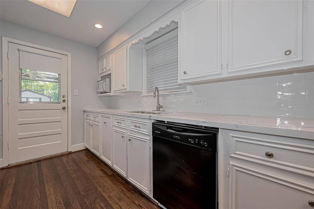 This spacious living room features hardwood floors, a large window with blinds for natural light, a ceiling fan, and a wall-mounted TV. The entryway has a stylish oval glass door, enhancing the home's charm.