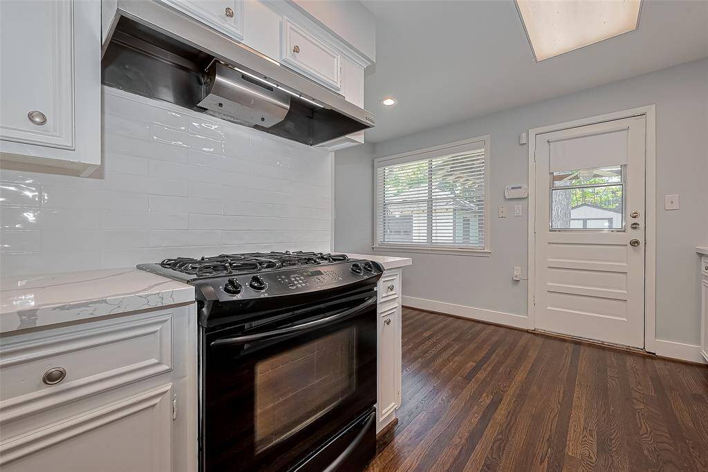 Bright, spacious kitchen with white cabinetry, quartz countertops, and dark wood flooring. Features include modern appliances, a gas stovetop, and ample storage, creating a sleek and functional cooking space.