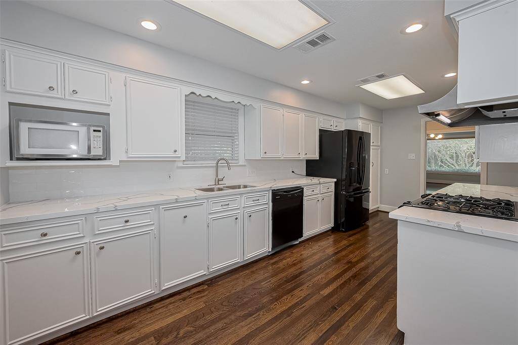This room features hardwood floors, neutral walls, and ample natural light from three large windows with wooden blinds. The space feels open and welcoming, perfect for a cozy living area or home office.