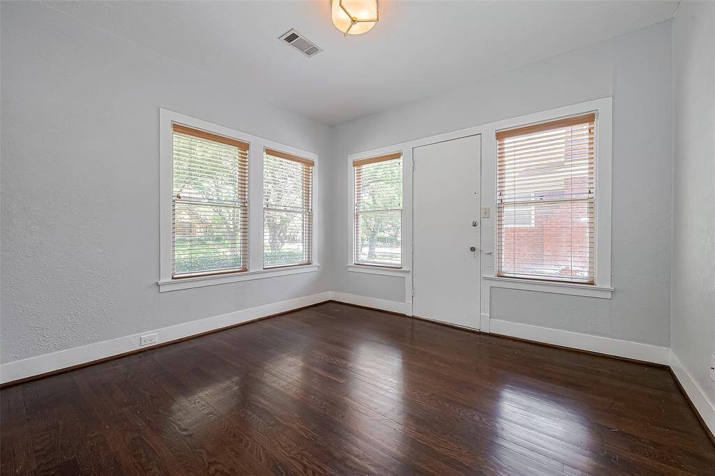 This spacious living area features rich hardwood floors, a ceiling fan, and a cozy fireplace flanked by built-in shelves. It opens into a bright adjoining room with ample natural light, perfect for dining or additional seating.