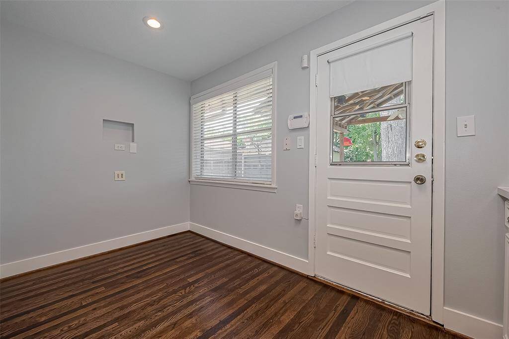 This photo shows a room with hardwood floors and light gray walls. There's a doorway leading to another room with a fireplace. A small closet with built-in shelves is visible, and natural light enters from a window in the adjacent room.