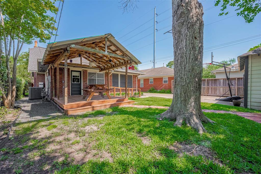 This backyard features a charming covered patio with a wooden deck and picnic table, ideal for outdoor dining. The space includes a neatly maintained lawn, a storage shed, and a view of the garage, all offering a cozy and functional outdoor living area.