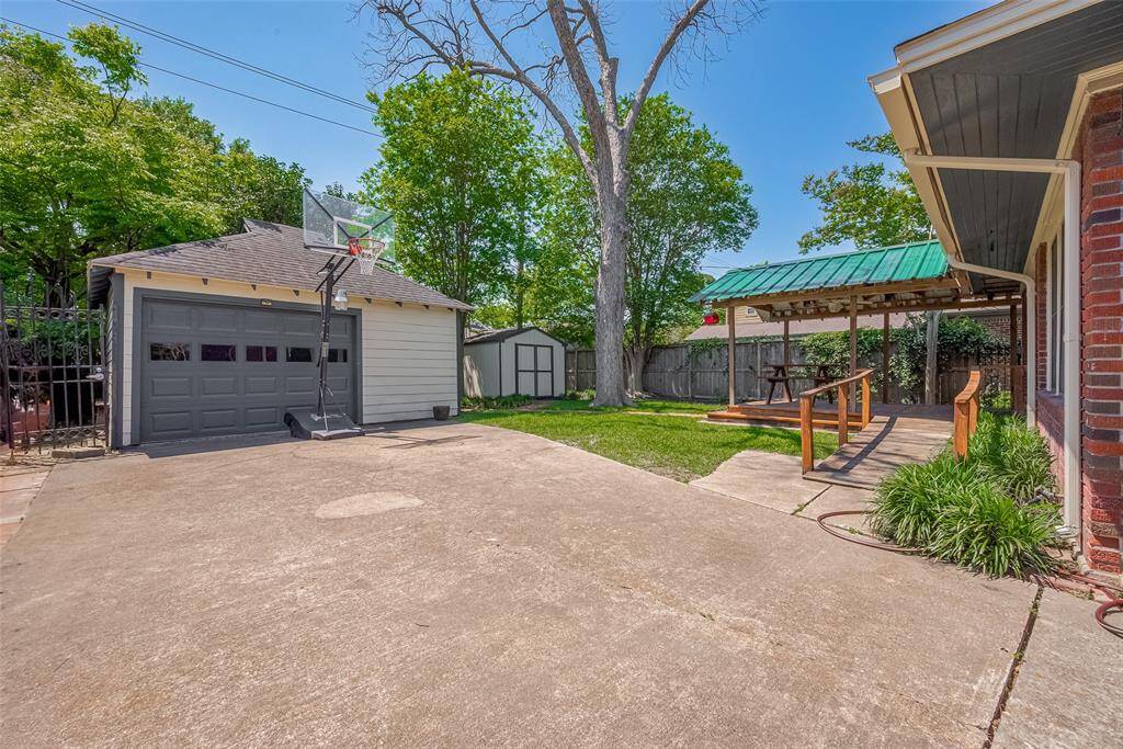 A charming backyard features a covered patio with a wooden ramp, perfect for outdoor dining. The yard includes a small shed, mature trees, and a well-maintained lawn, offering a serene and functional outdoor space.