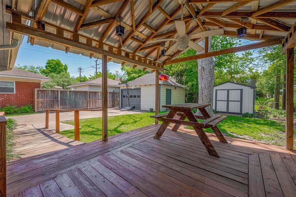 This charming backyard features a covered wooden deck with a picnic table, perfect for outdoor dining. The area is bordered by a well-maintained lawn and a brick path, ideal for relaxing and entertaining. The brick exterior of the house adds a classic touch.