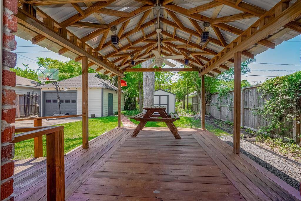 Charming backyard with a spacious lawn, mature tree, and a covered patio area perfect for outdoor dining. The red brick house and privacy fence create a cozy and inviting atmosphere.