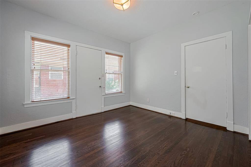 This photo showcases a spacious living room with hardwood floors, a ceiling fan, and a mounted TV. It opens into a dining area with modern lighting, leading to a bright kitchen. The space features neutral wall colors and ample natural light, creating a welcoming atmosphere.