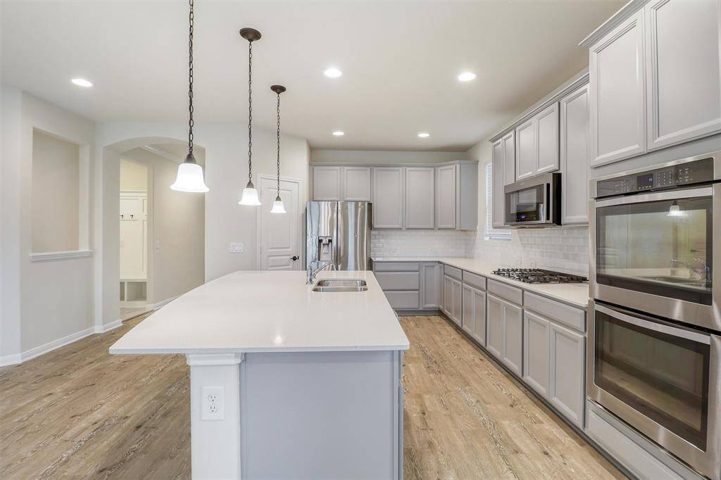 Additional features include a gas range with a built-in microwave above it, double ovens for added convenience, and a classic subway tile backsplash, adding both style and functionality to this chef's kitchen.