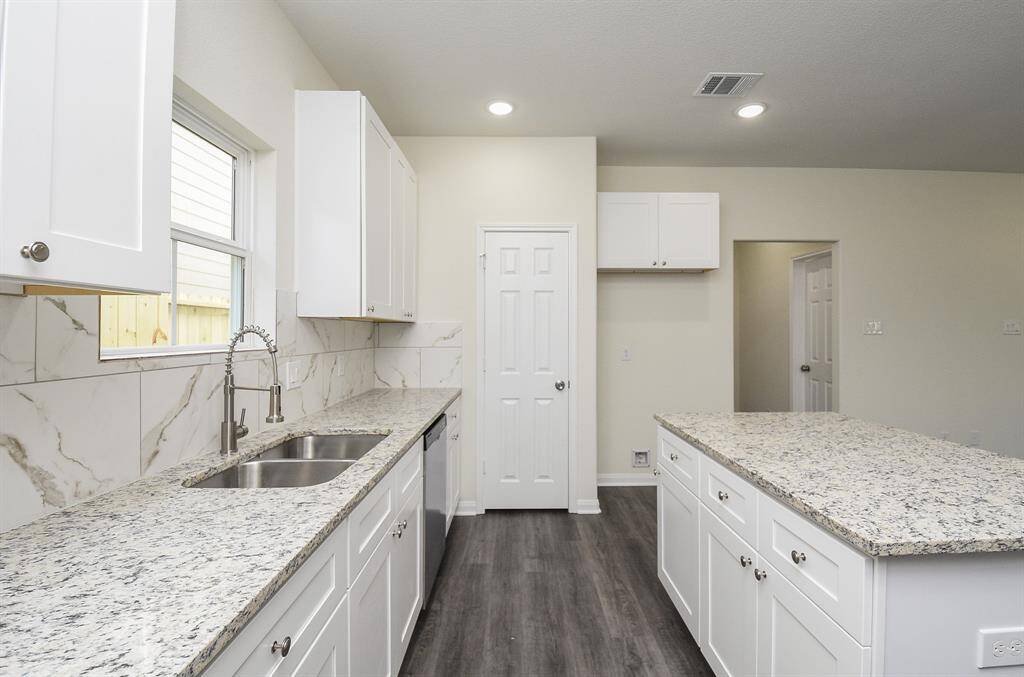 This is a modern kitchen featuring white cabinetry, granite countertops, and stainless-steel sink, with a window overlooking the backyard and wood-look flooring.