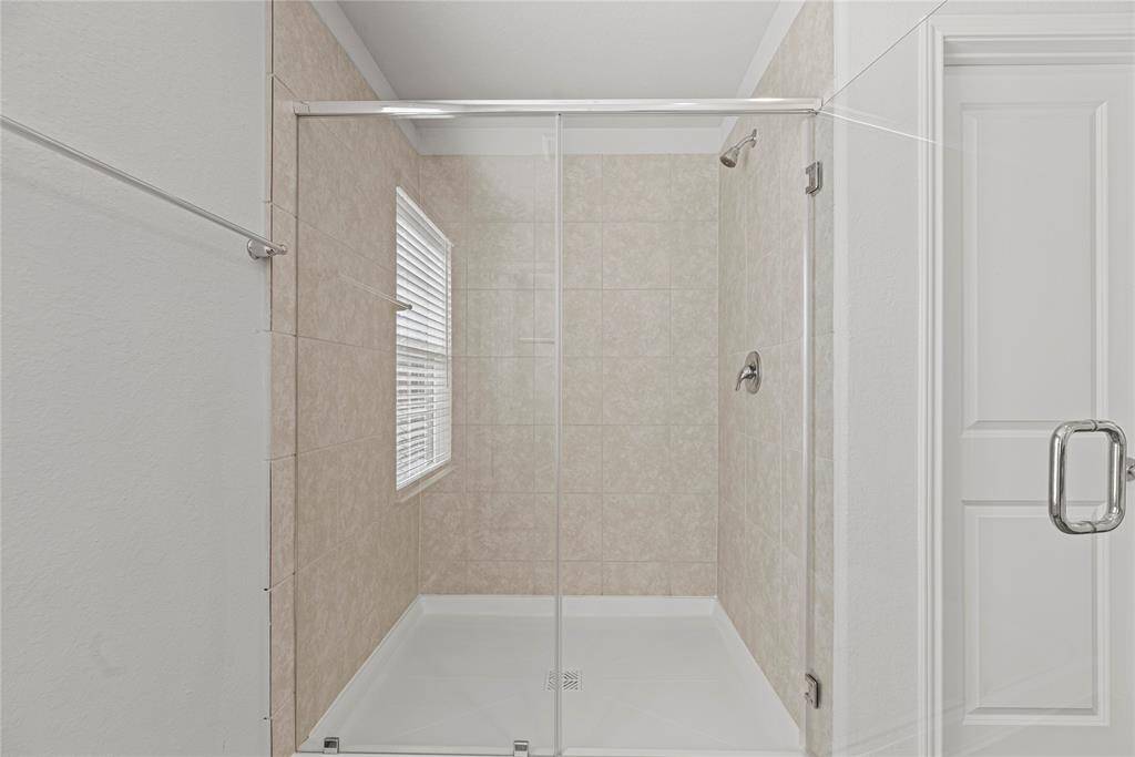 The primary bathroom also boasts aspacious walk-in shower,showcasing a neutral tile surroundthat extends to the ceiling. Theshower is elegantly enclosed by acustom glass partition for a modern,polished look.