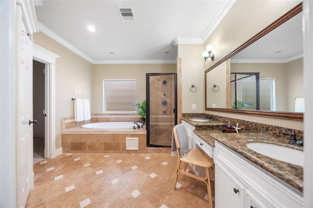 This spacious bathroom features a luxurious soaking tub and a separate glass-enclosed shower. It has dual sinks with granite countertops and ample storage. The neutral tile flooring and soft lighting create a relaxing atmosphere.