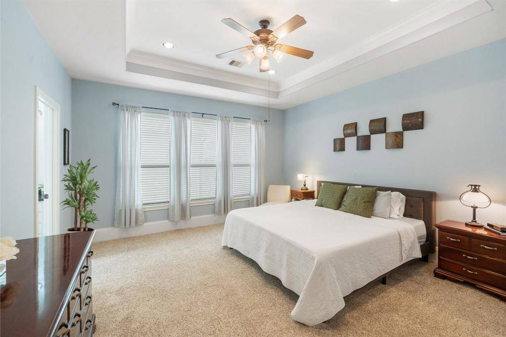 The primary retreat features a wall of windows that flood the room with natural light, complemented by a tray ceiling and plush carpet, creating a bright and inviting space.