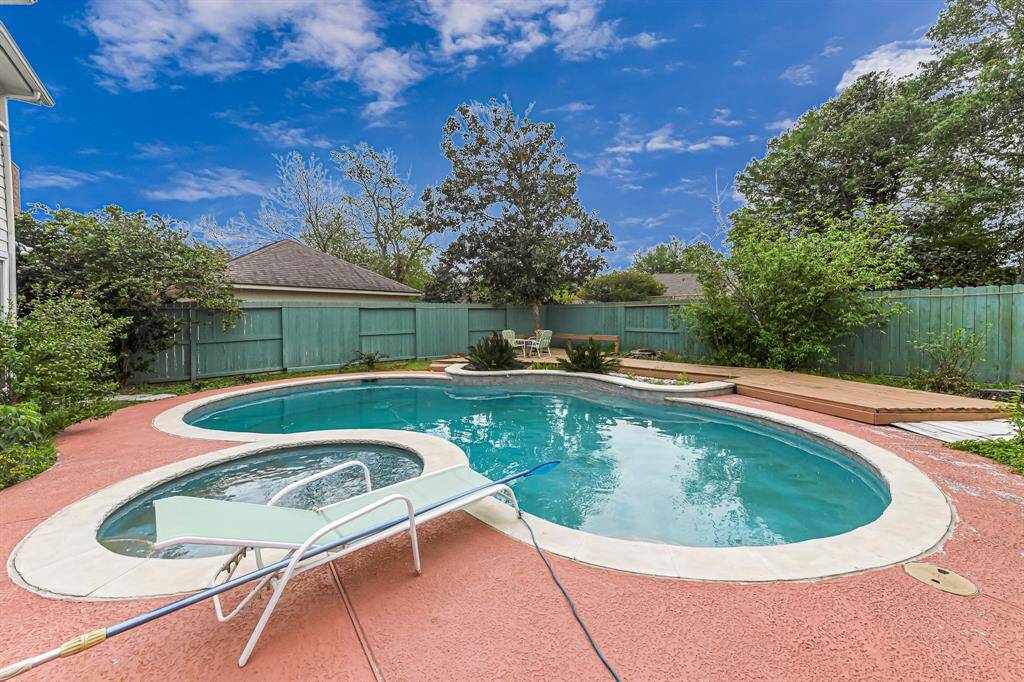 This backyard features a spacious, inviting pool with a surrounding patio area, perfect for relaxation and entertaining. The space is enclosed by a privacy fence and lush greenery, providing a serene and private oasis.