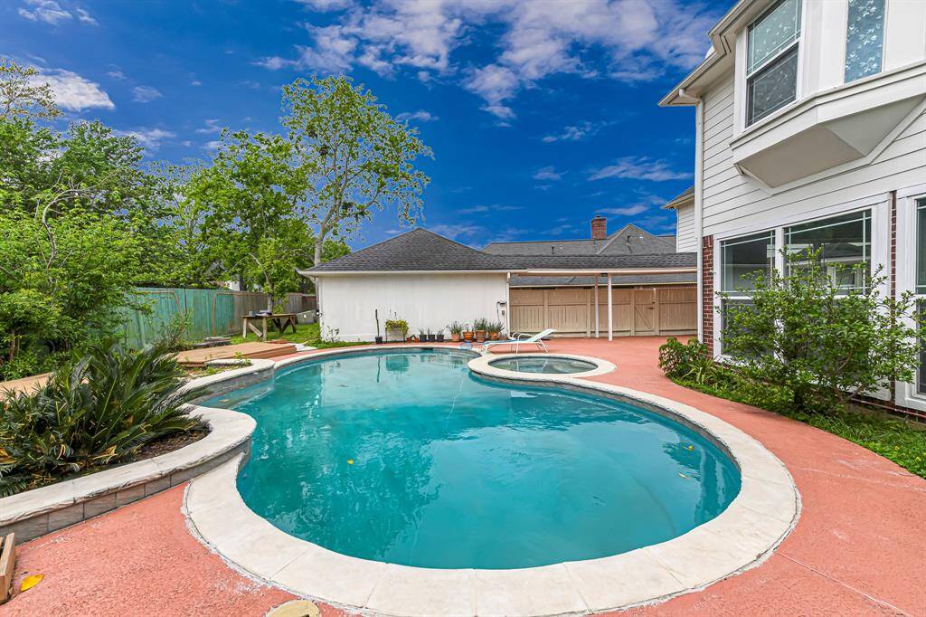 This photo showcases a spacious backyard with a large, inviting swimming pool and attached spa. It's surrounded by lush greenery, a privacy fence, and features a well-maintained patio area perfect for relaxation and outdoor activities.