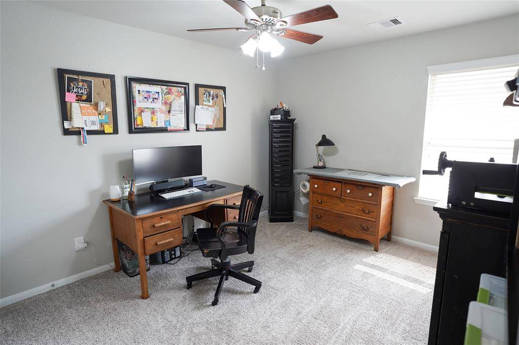 This is a bright, carpeted upstairs bedroom that is currently being used as a home office. This room features a ceiling fan, and natural light streaming through the window, which enhances this rooms inviting atmosphere.