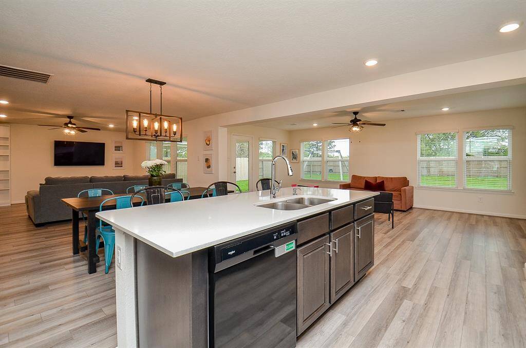 Bright and spacious sunroom with large windows overlooking a fenced backyard. Features include laminate flooring, a ceiling fan, and access to the patio through a glass door. The room is cozy with modern seating and a small play area.