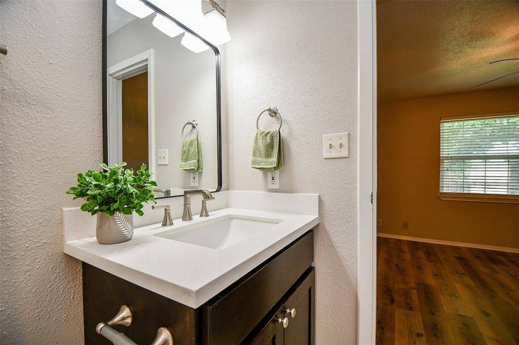 This photo features a modern bathroom with a sleek vanity and a large mirror. The room has neutral tones and a wood floor visible in the adjacent room, creating a warm and inviting atmosphere.