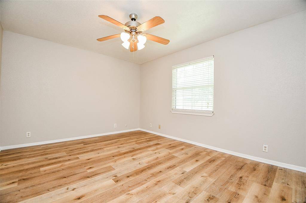 Bright, spacious room with light wood flooring, neutral walls, a ceiling fan, and a window that lets in natural light. Ideal for a bedroom or office.
