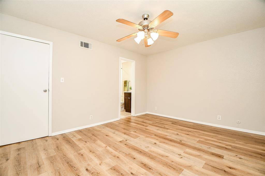 This is a bright, spacious room with light wood flooring and neutral walls. It features a ceiling fan with lights and an adjoining door that leads to another area, possibly a bathroom. Ideal for a bedroom or home office.