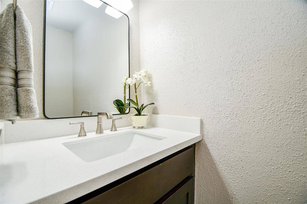 This bathroom features a modern design with a sleek white countertop and integrated sink, complemented by a large mirror and contemporary fixtures. A small plant adds a touch of elegance.