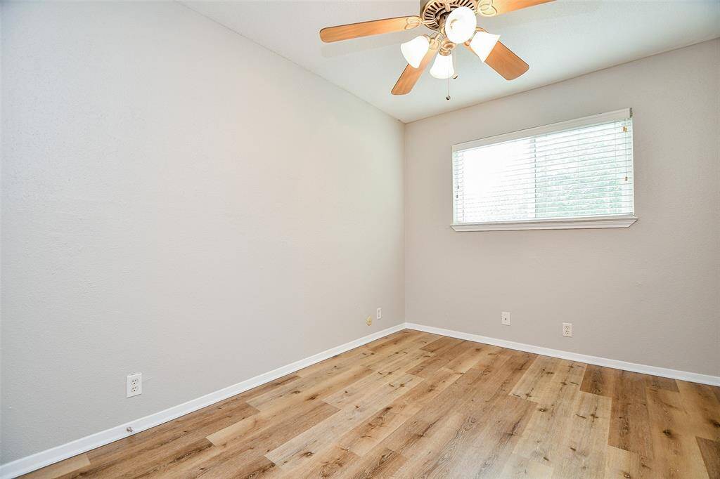This room features light wood flooring, neutral walls, a ceiling fan with lights, and a window with blinds allowing natural light to brighten the space. Perfect for a cozy bedroom or office.